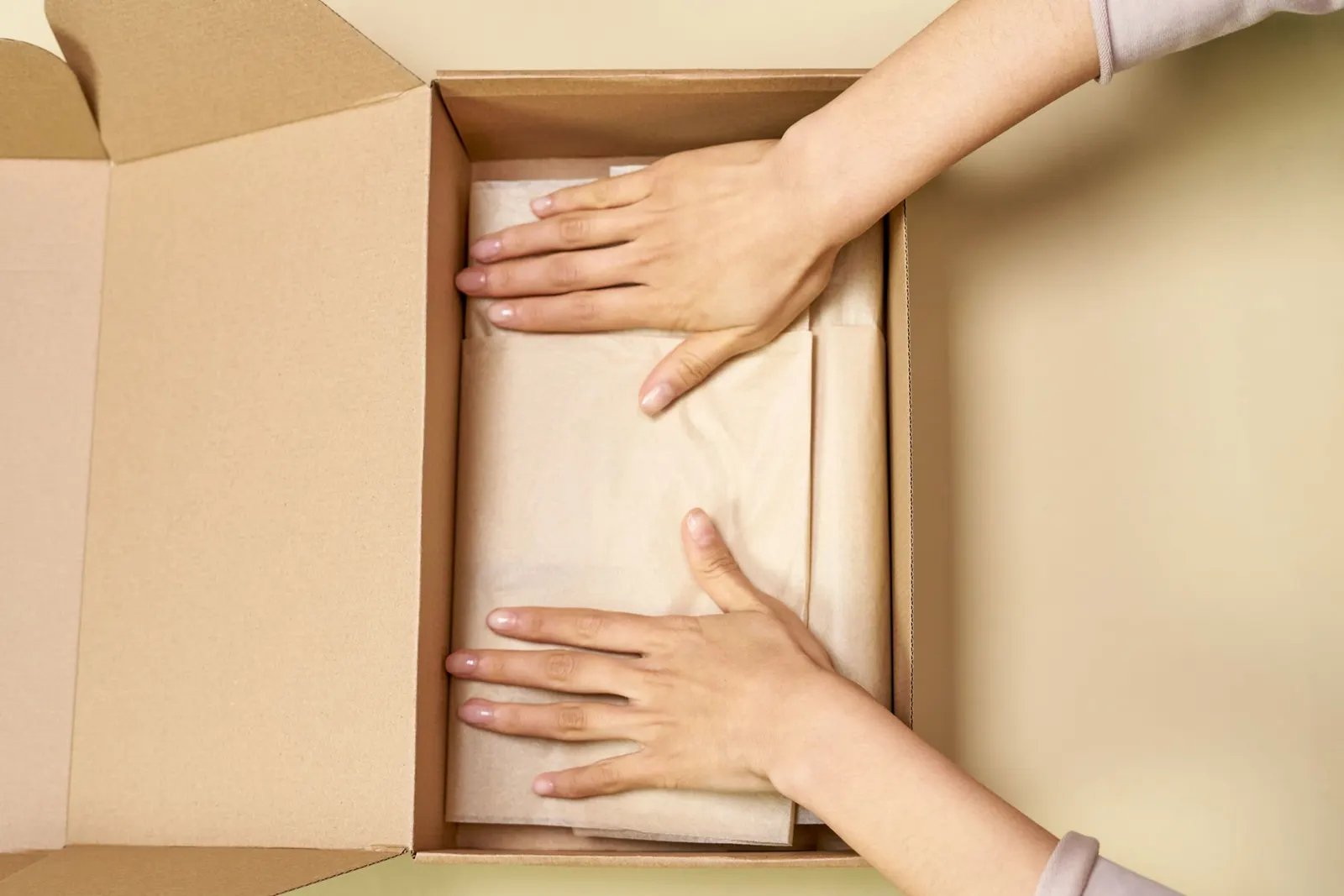 Hands opening a plain cardboard parcel lined with tissue paper.
