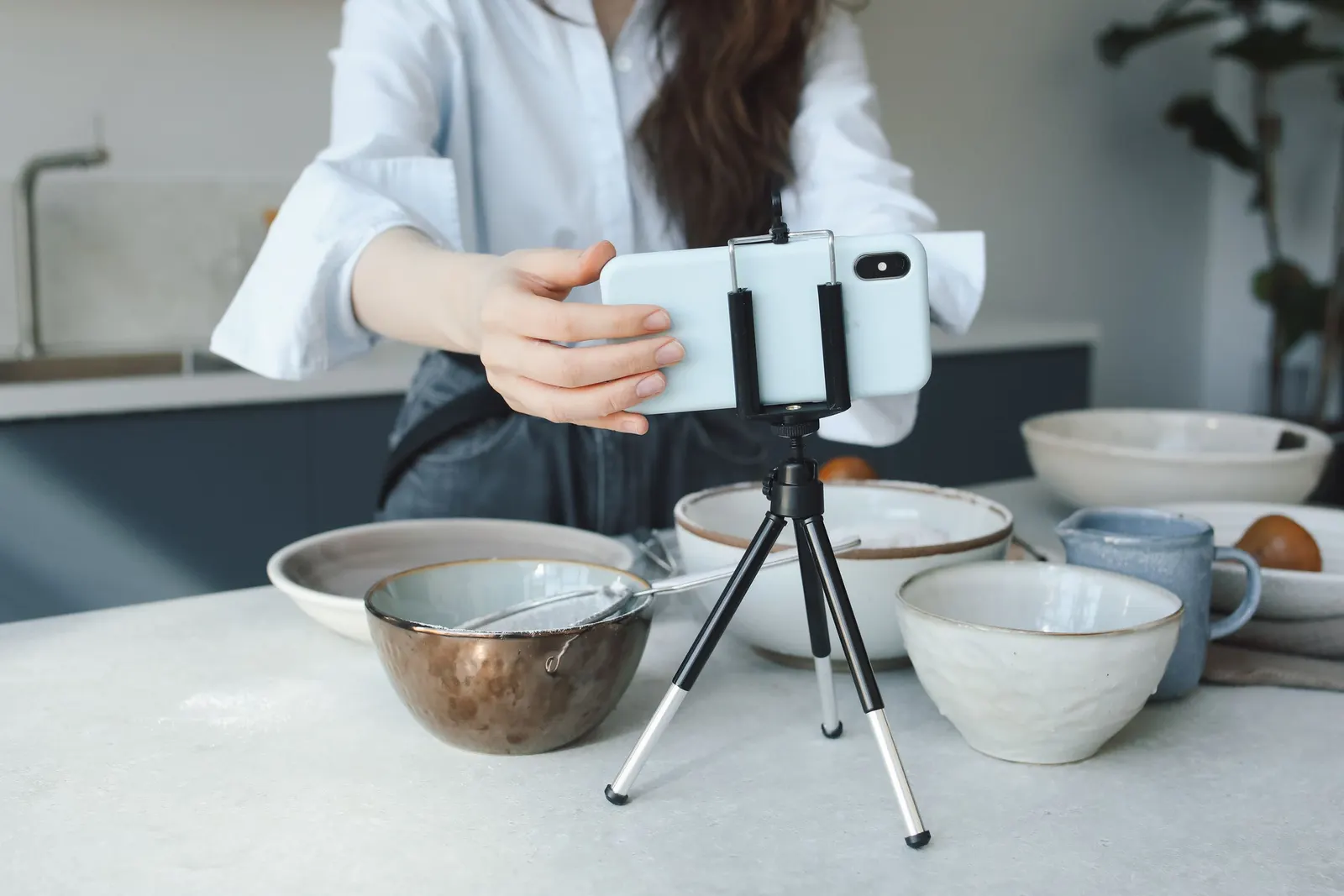 A creator sets a phone on a small tripod above a kitchen counter, ready to film.