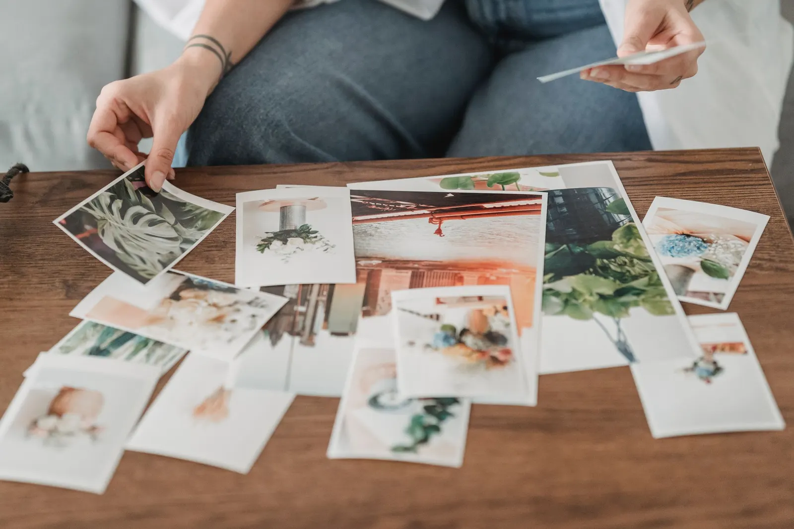 Hands choose printed photos of plants and flowers spread on a wooden table.