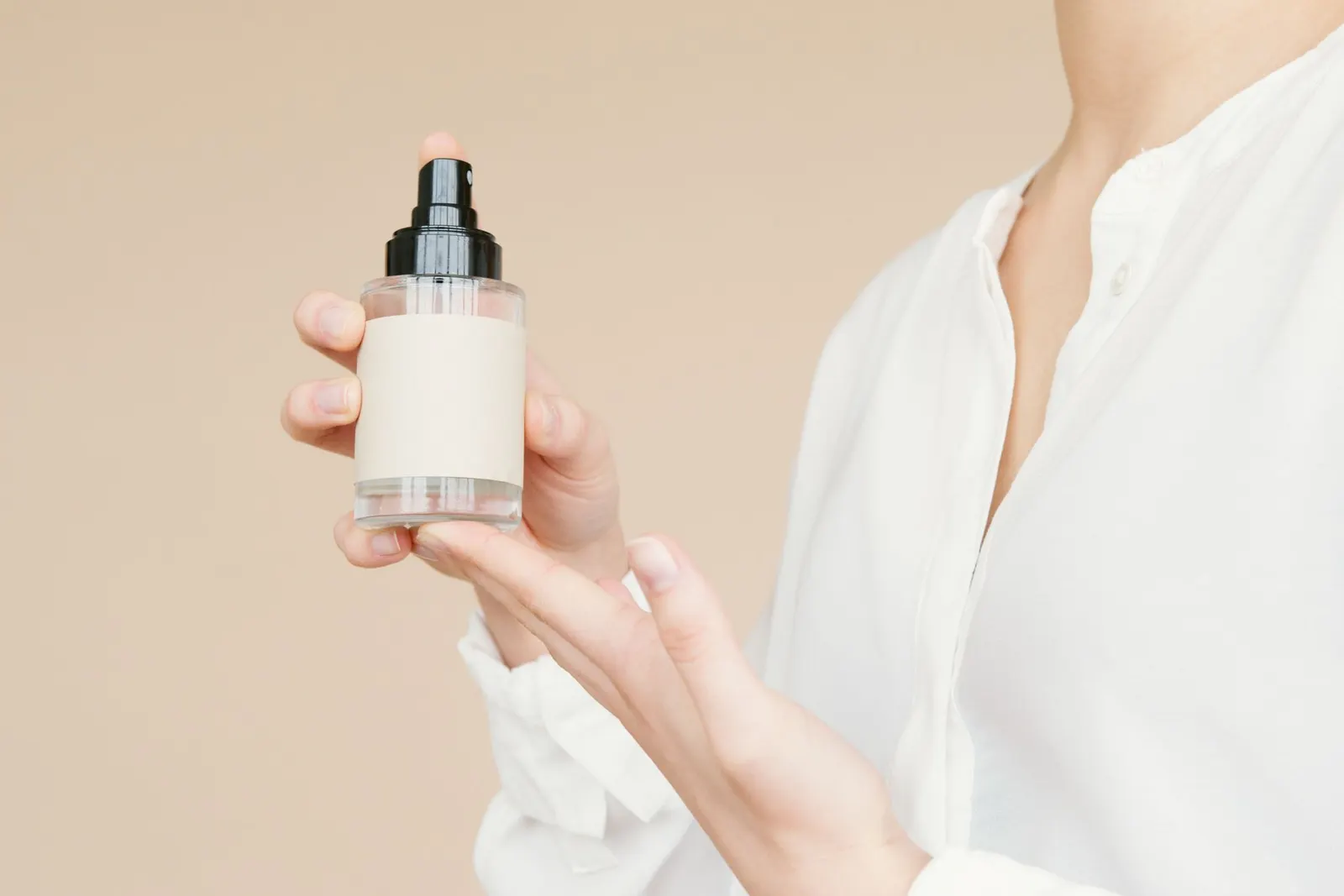Hands hold a small bottle with a blank label up to the camera.