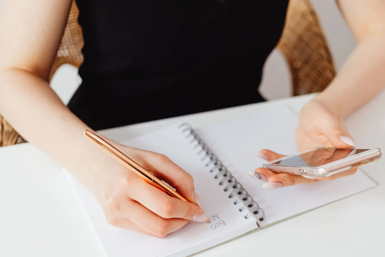 A creator notes figures in a notebook while checking a phone.